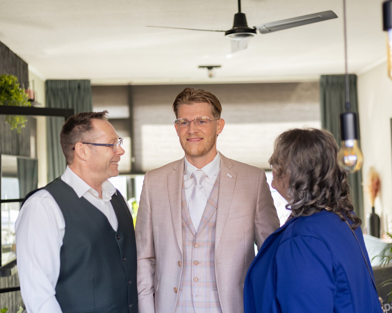 Bruidegom in licht pak deelt een ontspannen moment met zijn ouders op de trouwochtend, bruidsfotografie door Amped Productions
